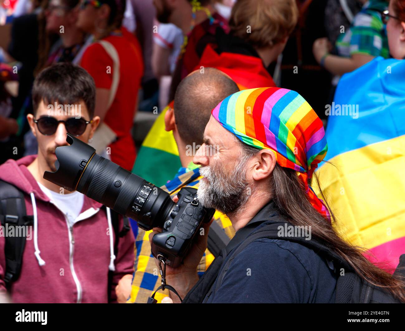 Photographe avec un bandana arc-en-ciel coloré Pride capture la foule vibrante lors d'un événement de fierté de birmingham avec un appareil photo reflex numérique professionnel Banque D'Images
