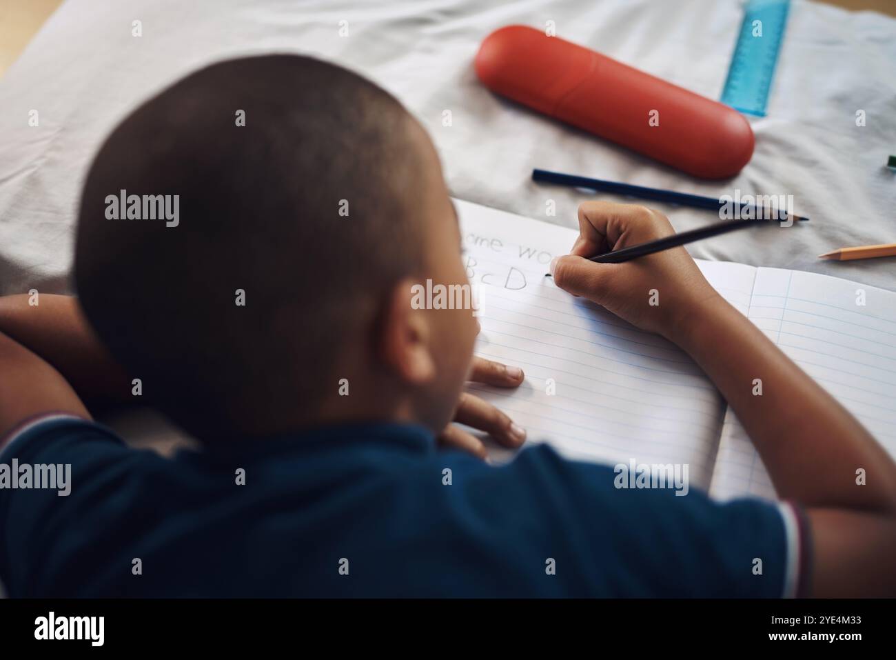 Garçon, couché et écrit avec un livre dans la chambre pour la créativité, la littérature ou le dessin pour l'activité éducative à la maison. Jeune, homme ou enfant Banque D'Images