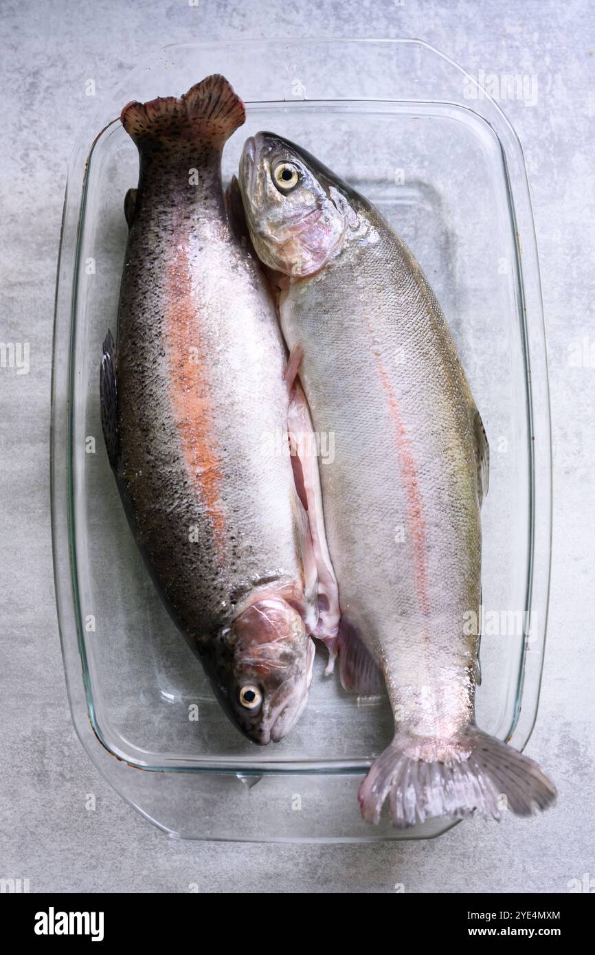 Deux poissons de truite frais sur une plaque de verre sur la table de cuisine gros plan. Photographie culinaire Banque D'Images
