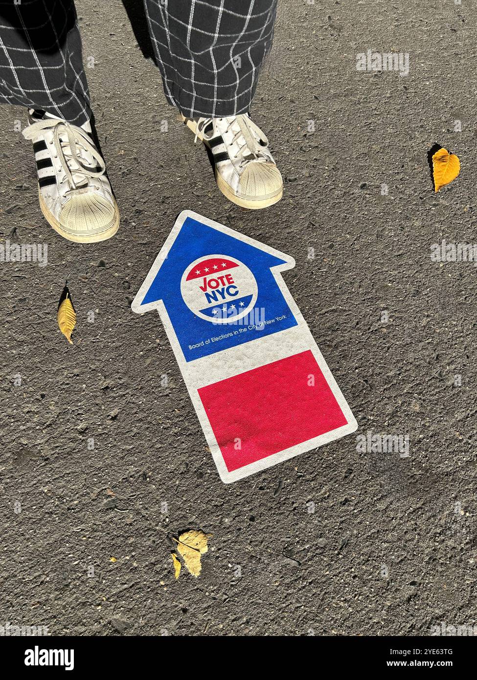 Vue à angle élevé d'une personne debout près du conseil d'administration des élections de New York signe de flèche de vote anticipé adhéré au trottoir, New York City, New York, États-Unis Banque D'Images