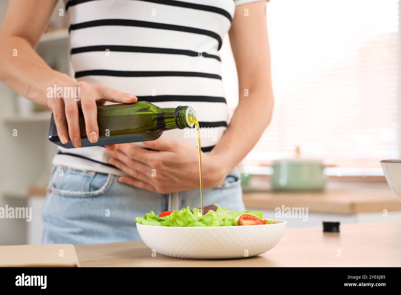 Jeune femme enceinte versant de l'huile dans une salade de légumes dans la cuisine, gros plan Banque D'Images