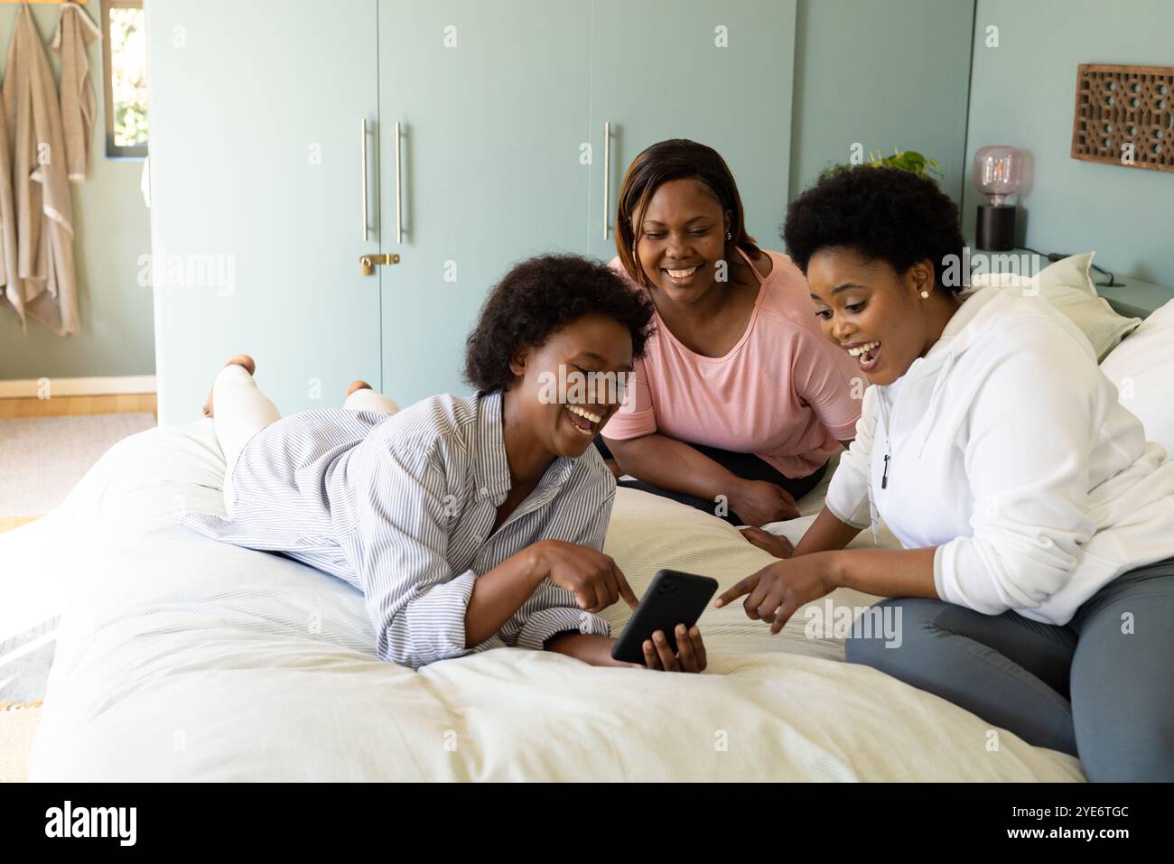 Amies afro-américaines riant et partageant des moments sur smartphone tout en se relaxant à la maison Banque D'Images