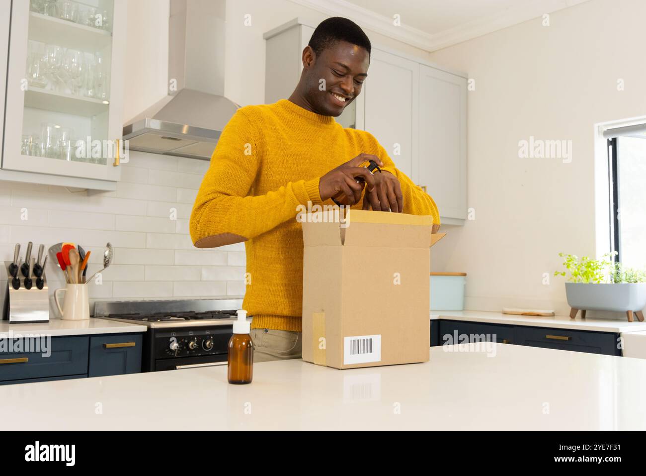 Homme afro-américain souriant dans le paquet d'ouverture de cuisine avec des huiles essentielles, à la maison Banque D'Images