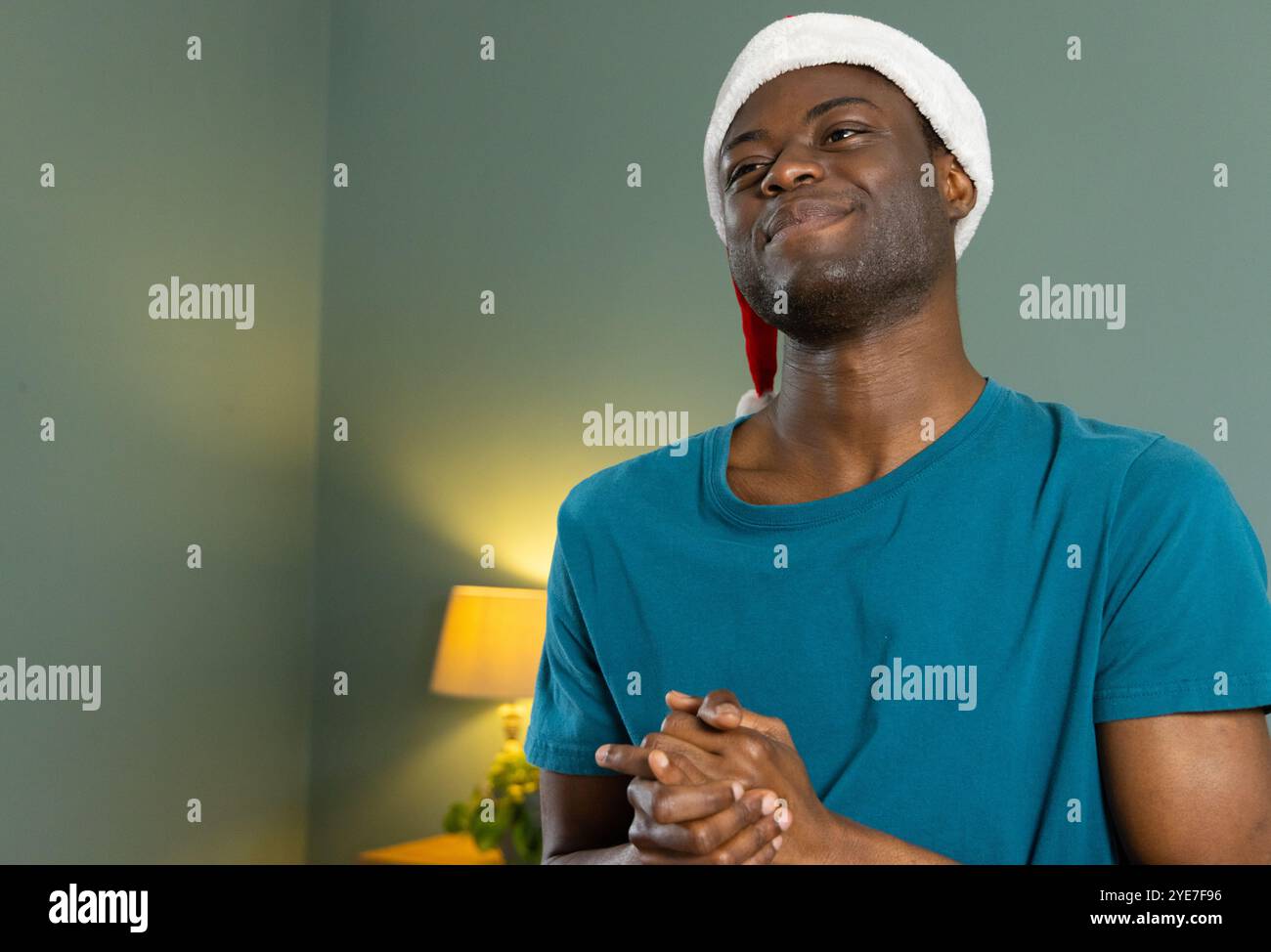 Noël, souriant homme afro-américain portant chapeau de Père Noël profitant d'un moment festif à la maison Banque D'Images