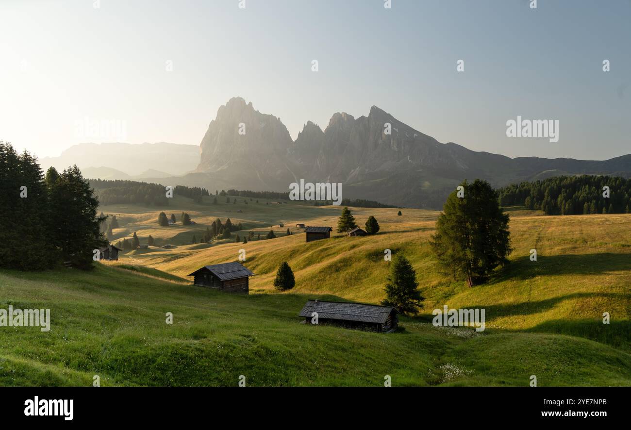 Lever de soleil sur Alpe di Siusi, Tyrol du Sud, Italie, avec des cabanes traditionnelles et le massif du Sassolungo. La lumière dorée baigne les prairies alpines. Banque D'Images