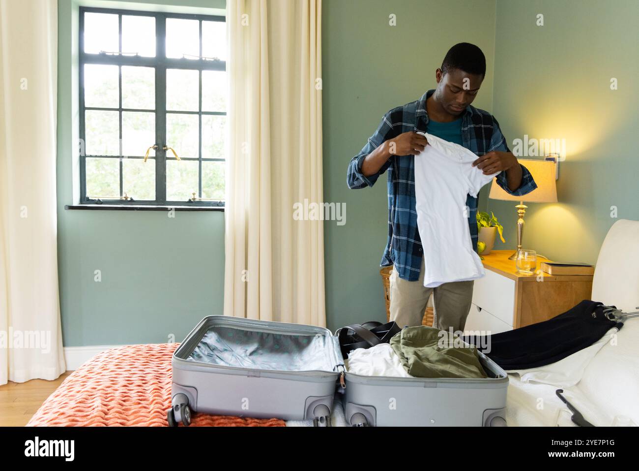 Homme afro-américain emballant la valise dans la chambre, préparant le voyage de vacances, à la maison Banque D'Images