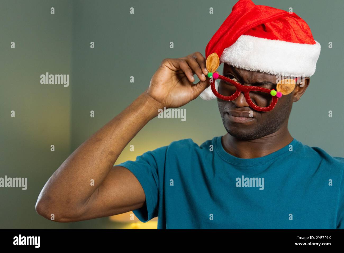 Noël, homme afro-américain portant chapeau de père noël ajustant les lunettes de fête à la maison Banque D'Images