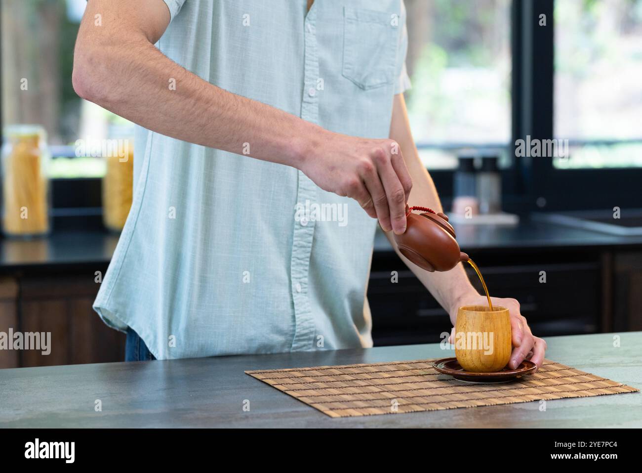 Verser le thé dans une tasse en bois dans la cuisine, l'homme profitant d'un moment paisible, à la maison Banque D'Images