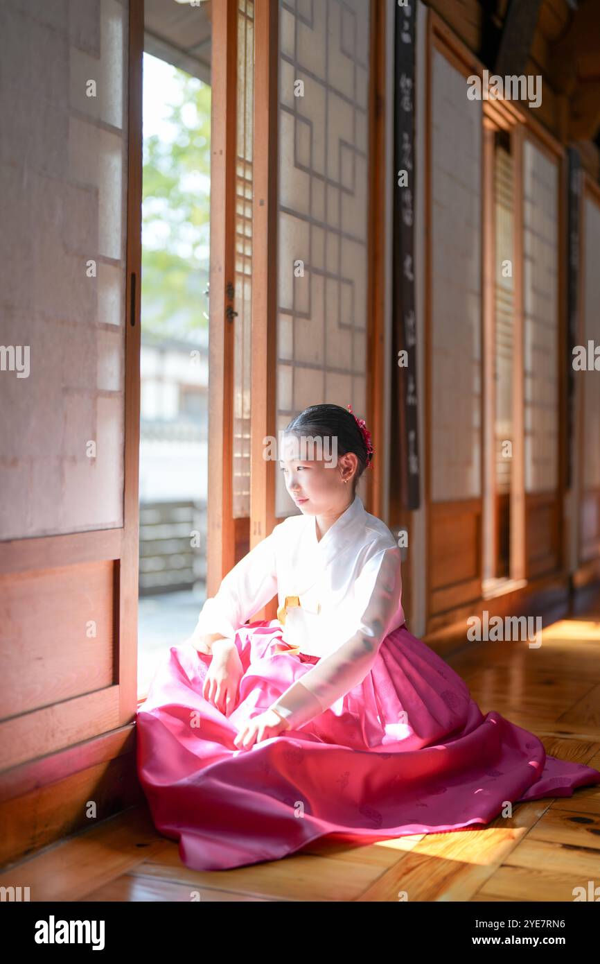 Une jeune coréenne de 9 ans portant un hanbok se tient debout à l'intérieur d'un bâtiment traditionnel, regardant comme le soleil coule dedans, dans la ville historique de Gyedo Banque D'Images