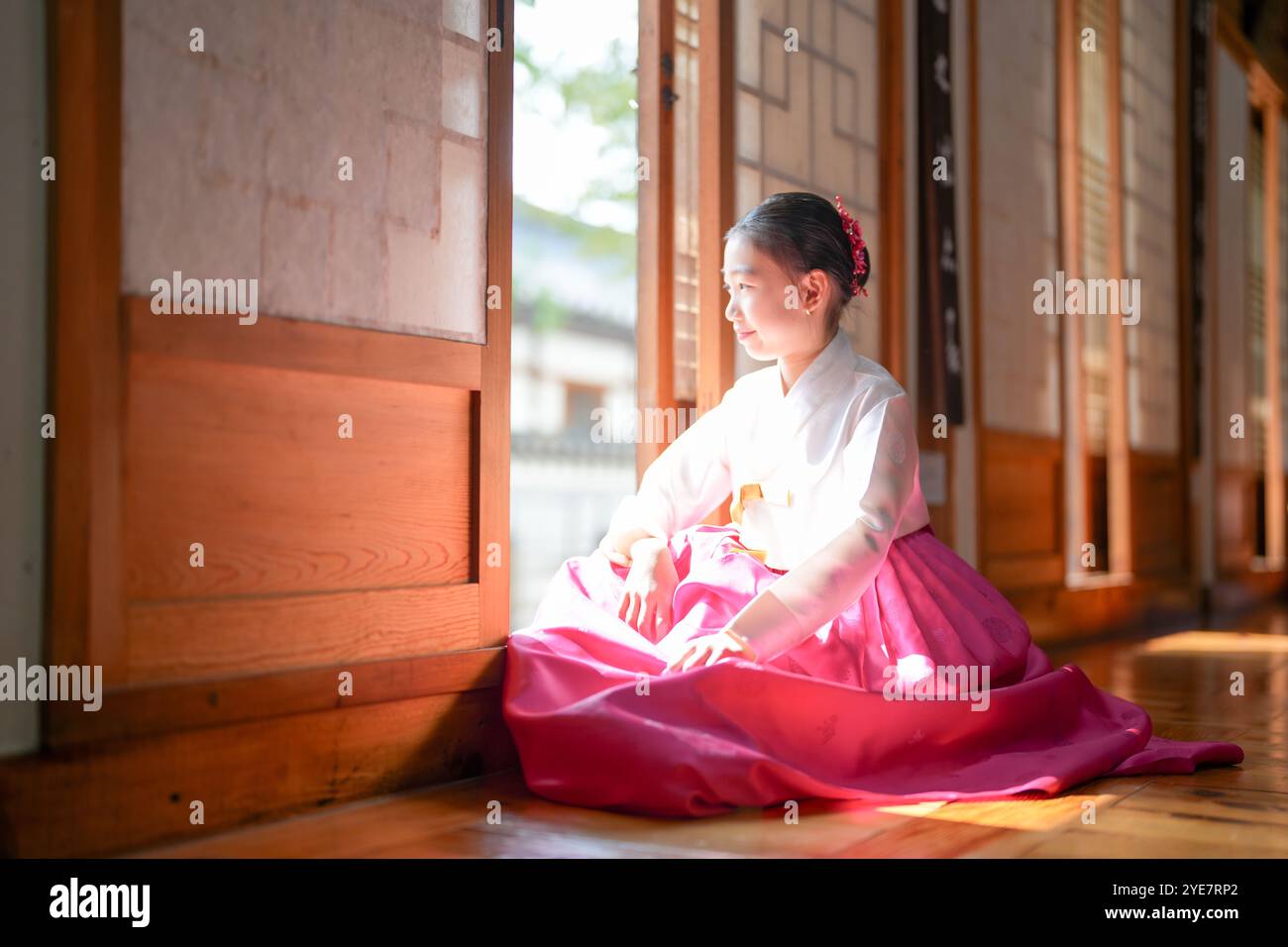 Une jeune coréenne de 9 ans portant un hanbok se tient debout à l'intérieur d'un bâtiment traditionnel, regardant comme le soleil coule dedans, dans la ville historique de Gyedo Banque D'Images