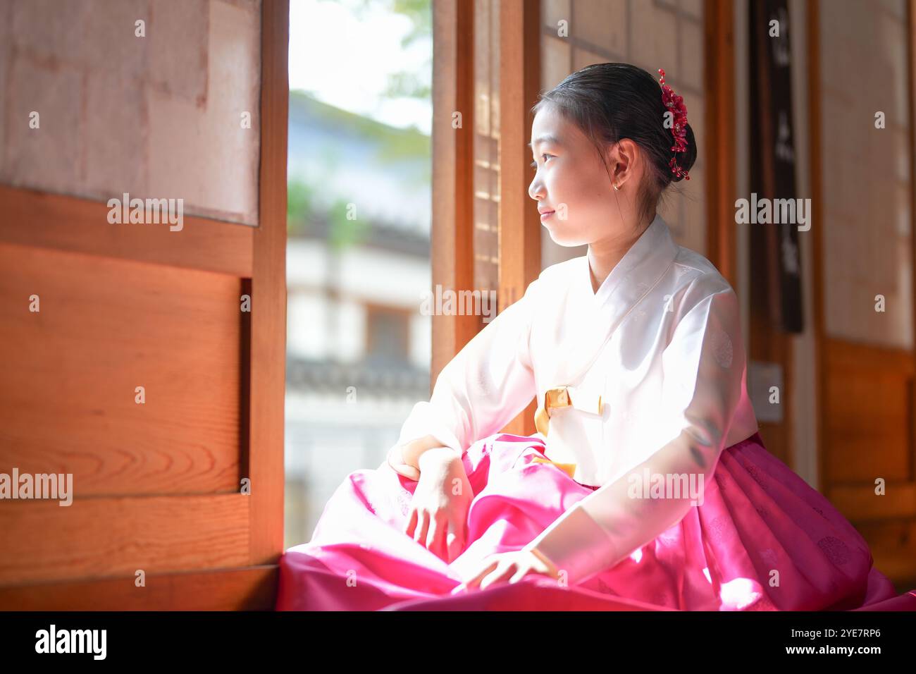 Une jeune coréenne de 9 ans portant un hanbok se tient debout à l'intérieur d'un bâtiment traditionnel, regardant comme le soleil coule dedans, dans la ville historique de Gyedo Banque D'Images