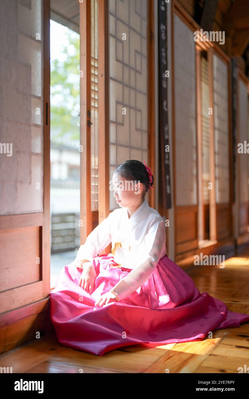Une jeune coréenne de 9 ans portant un hanbok se tient debout à l'intérieur d'un bâtiment traditionnel, regardant comme le soleil coule dedans, dans la ville historique de Gyedo Banque D'Images