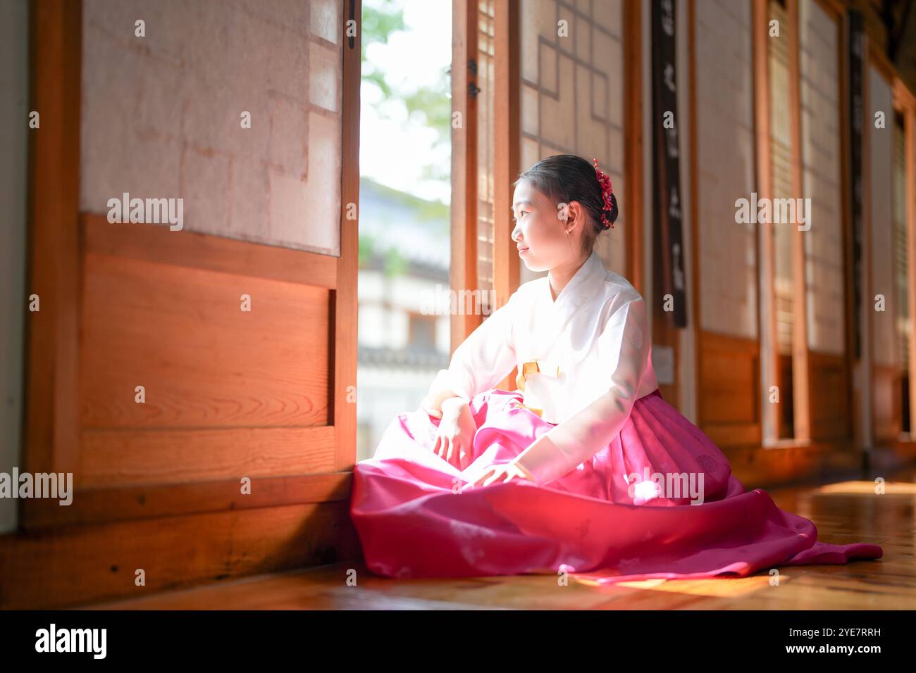 Une jeune coréenne de 9 ans portant un hanbok se tient debout à l'intérieur d'un bâtiment traditionnel, regardant comme le soleil coule dedans, dans la ville historique de Gyedo Banque D'Images