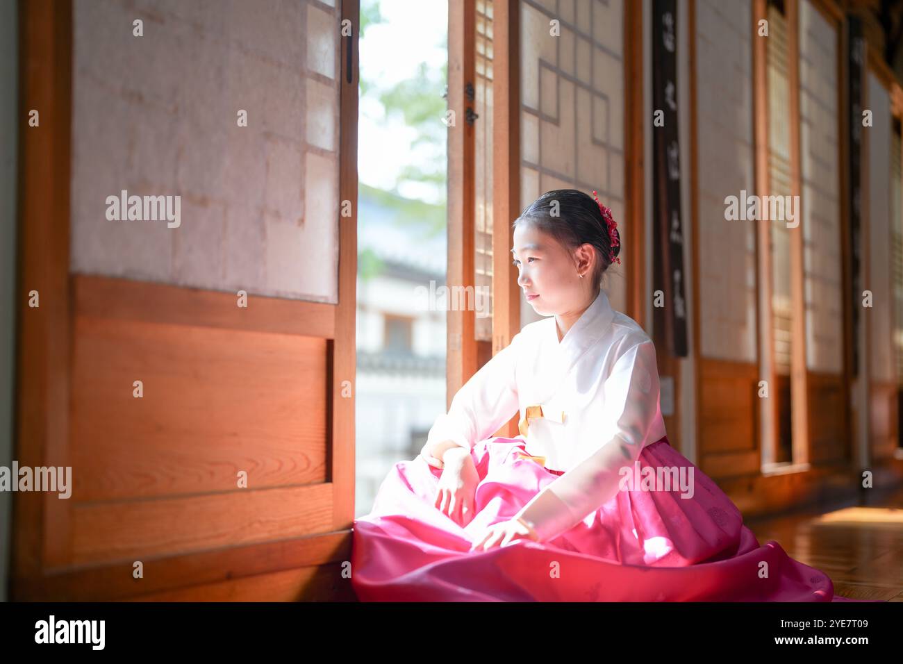 Une jeune coréenne de 9 ans portant un hanbok se tient debout à l'intérieur d'un bâtiment traditionnel, regardant comme le soleil coule dedans, dans la ville historique de Gyedo Banque D'Images