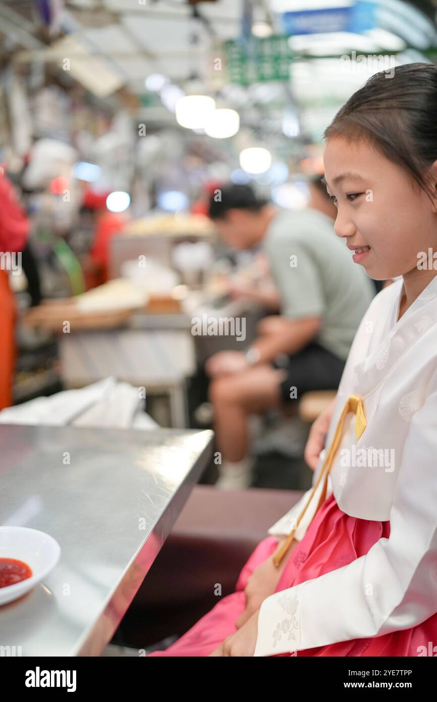 Une jeune coréenne de 9 ans portant un hanbok mange un repas dans un marché local de Changgyeonggung-ro, district de Jongno, Séoul, Corée. Banque D'Images