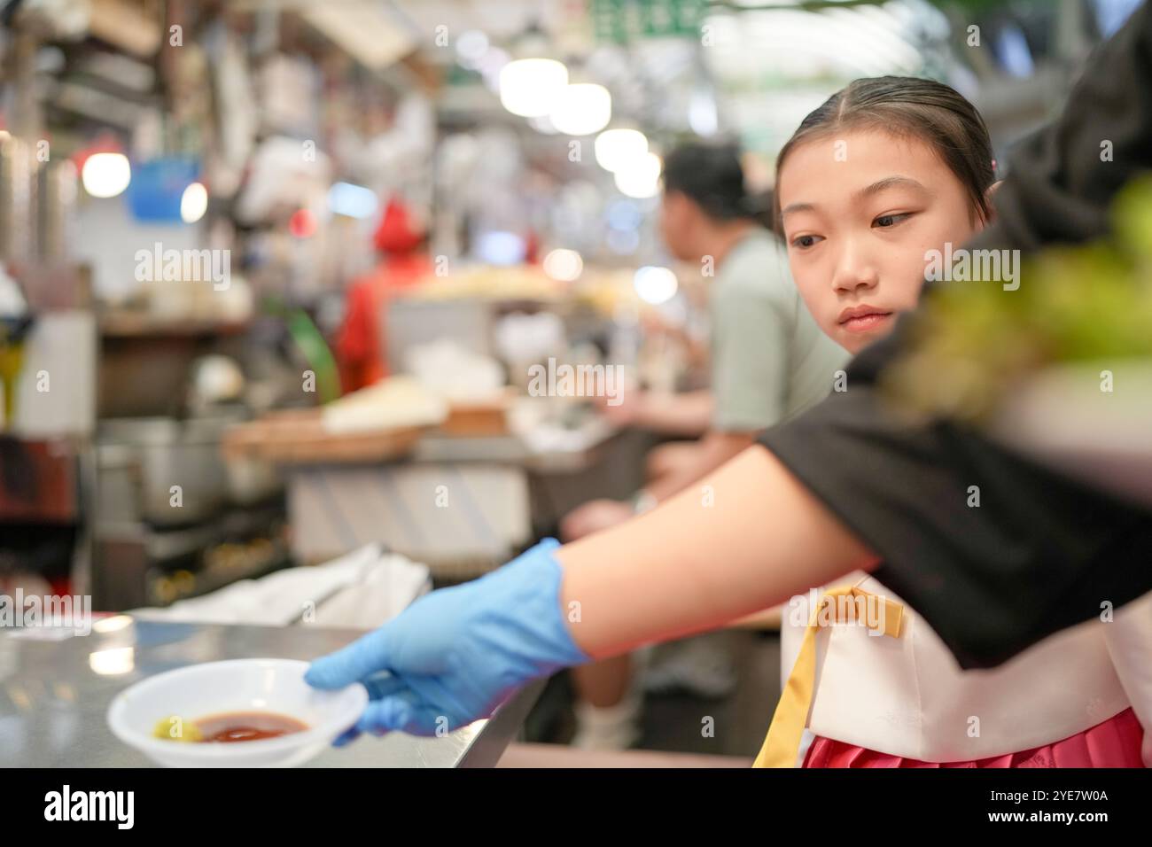 Une jeune coréenne de 9 ans portant un hanbok mange un repas dans un marché local de Changgyeonggung-ro, district de Jongno, Séoul, Corée. Banque D'Images