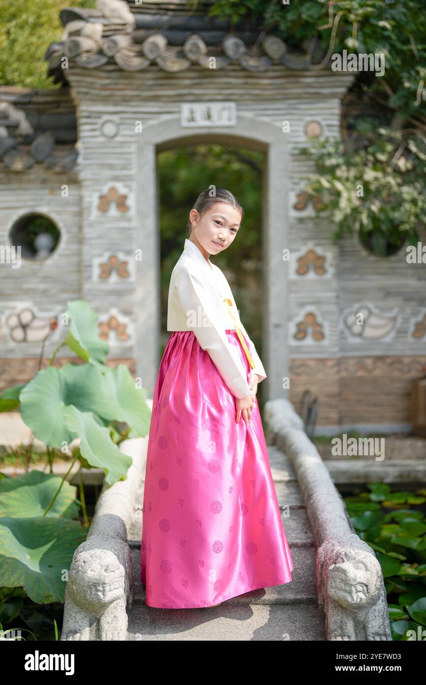 Une jeune coréenne de 9 ans portant un hanbok se tient devant une porte traditionnelle, la regardant dans la ville historique de Gyedong-gil, Jongno Distric Banque D'Images