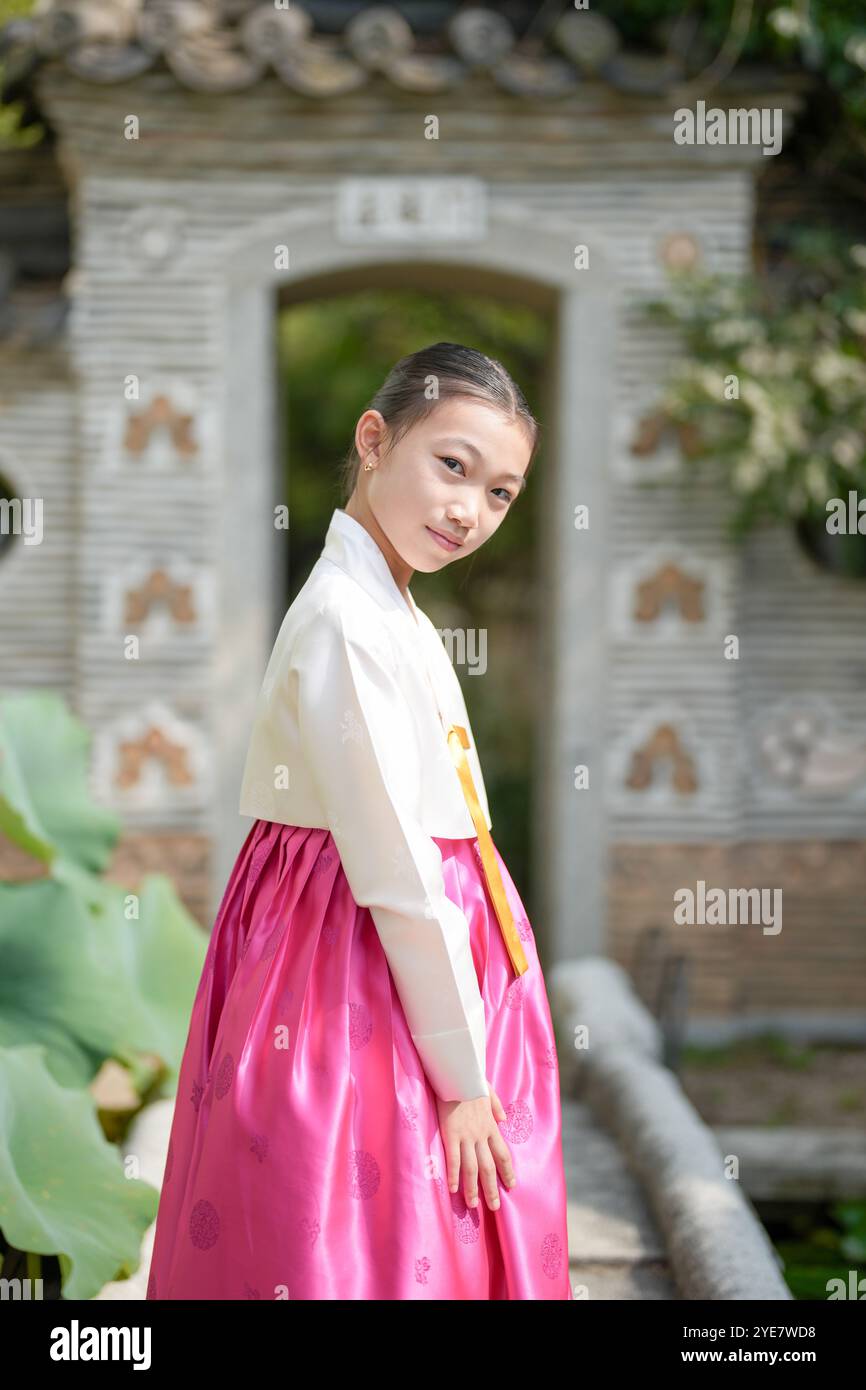 Une jeune coréenne de 9 ans portant un hanbok se tient devant une porte traditionnelle, la regardant dans la ville historique de Gyedong-gil, Jongno Distric Banque D'Images