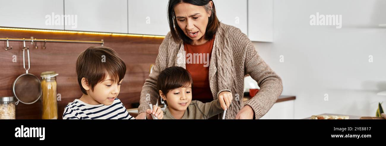 Une grand-mère se délecte de préparer des friandises de vacances avec ses deux petits-fils joyeux, célébrant la joie de l'hiver ensemble. Banque D'Images