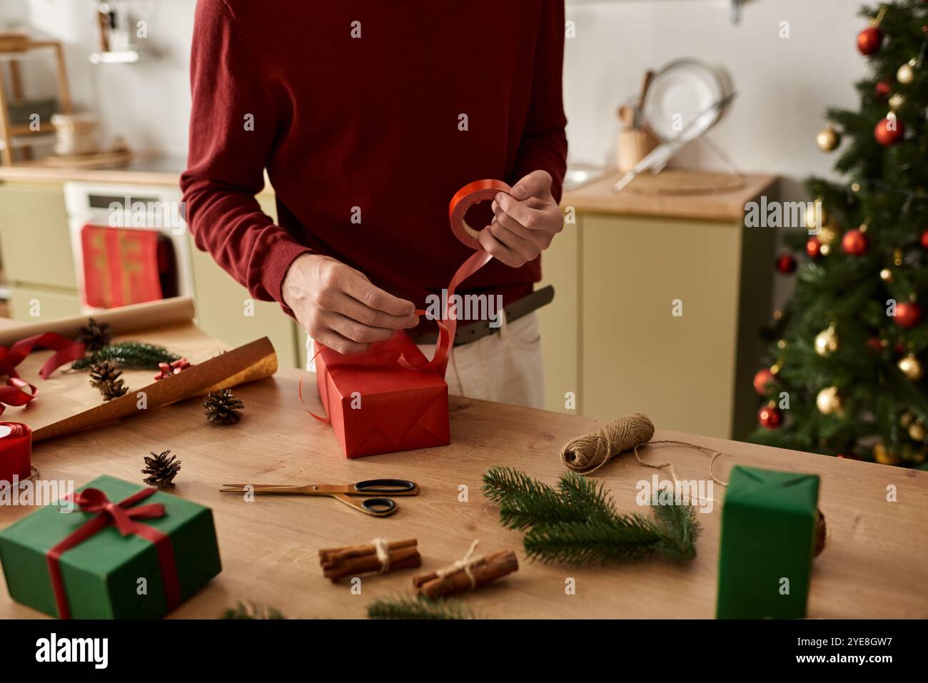 Le jeune homme enveloppe soigneusement les cadeaux festifs tout en étant entouré de décorations de Noël et de joie. Banque D'Images