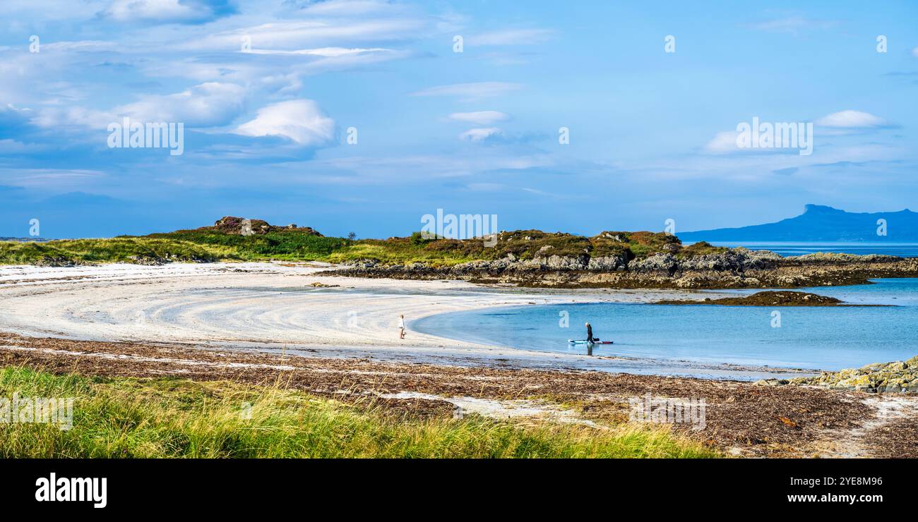 Promeneur de chiens et paddleboarder sur Traigh Beach près de Portnaluchaig à Lochaber, Highlands écossais, Écosse, avec l'île d'Eigg au loin Banque D'Images