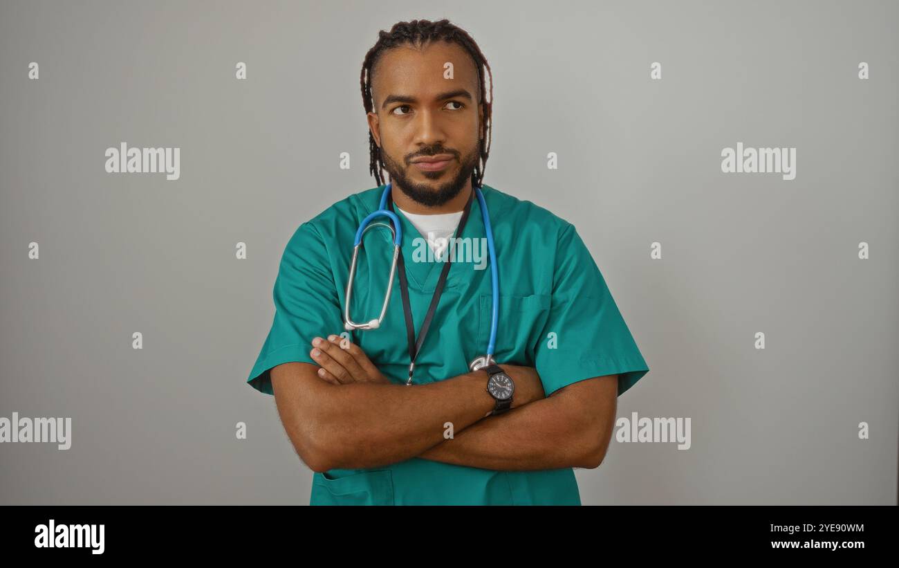 Jeune homme africain confiant avec des tresses dans des gommages verts debout isolé contre un mur blanc avec les bras croisés et un stéthoscope autour du cou exsudant Banque D'Images