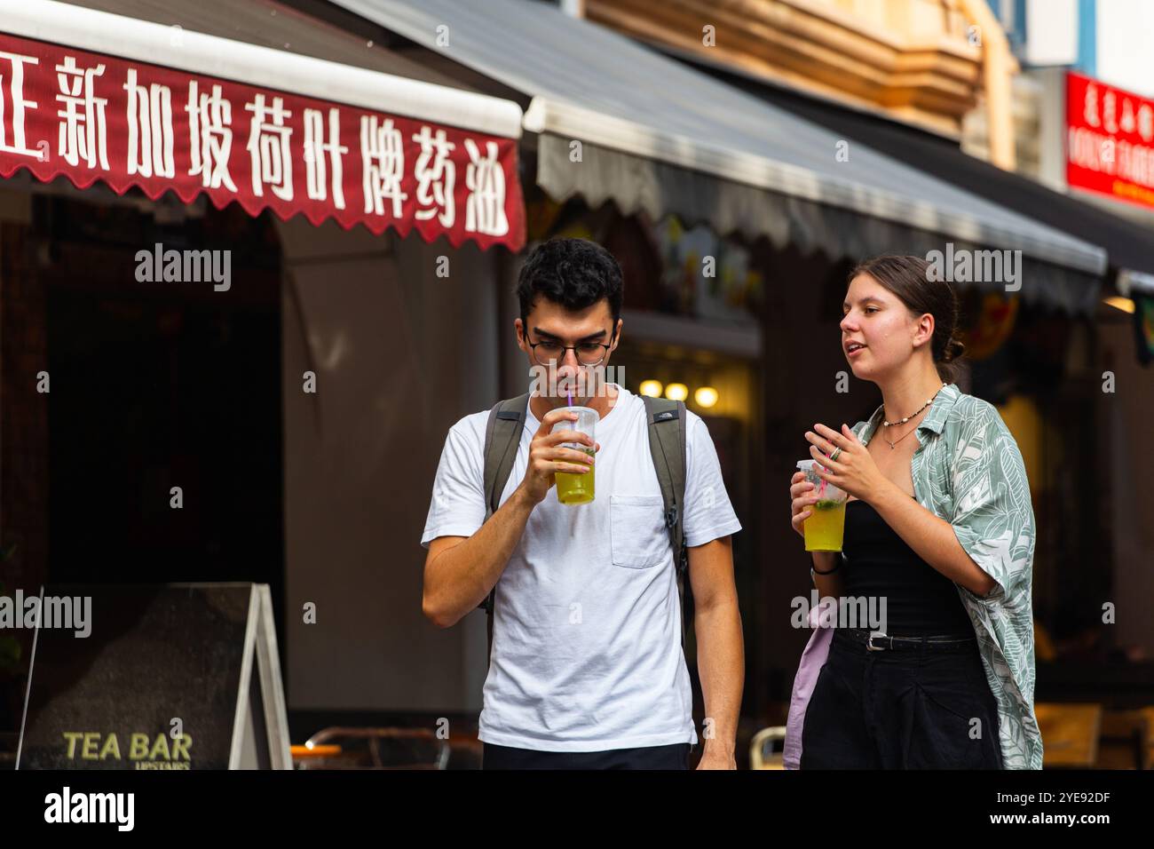 Un couple de touristes buvant du jus pour étancher la soif de s'hydrater dans le temps chaud et humide, Chinatown, Singapour. Banque D'Images