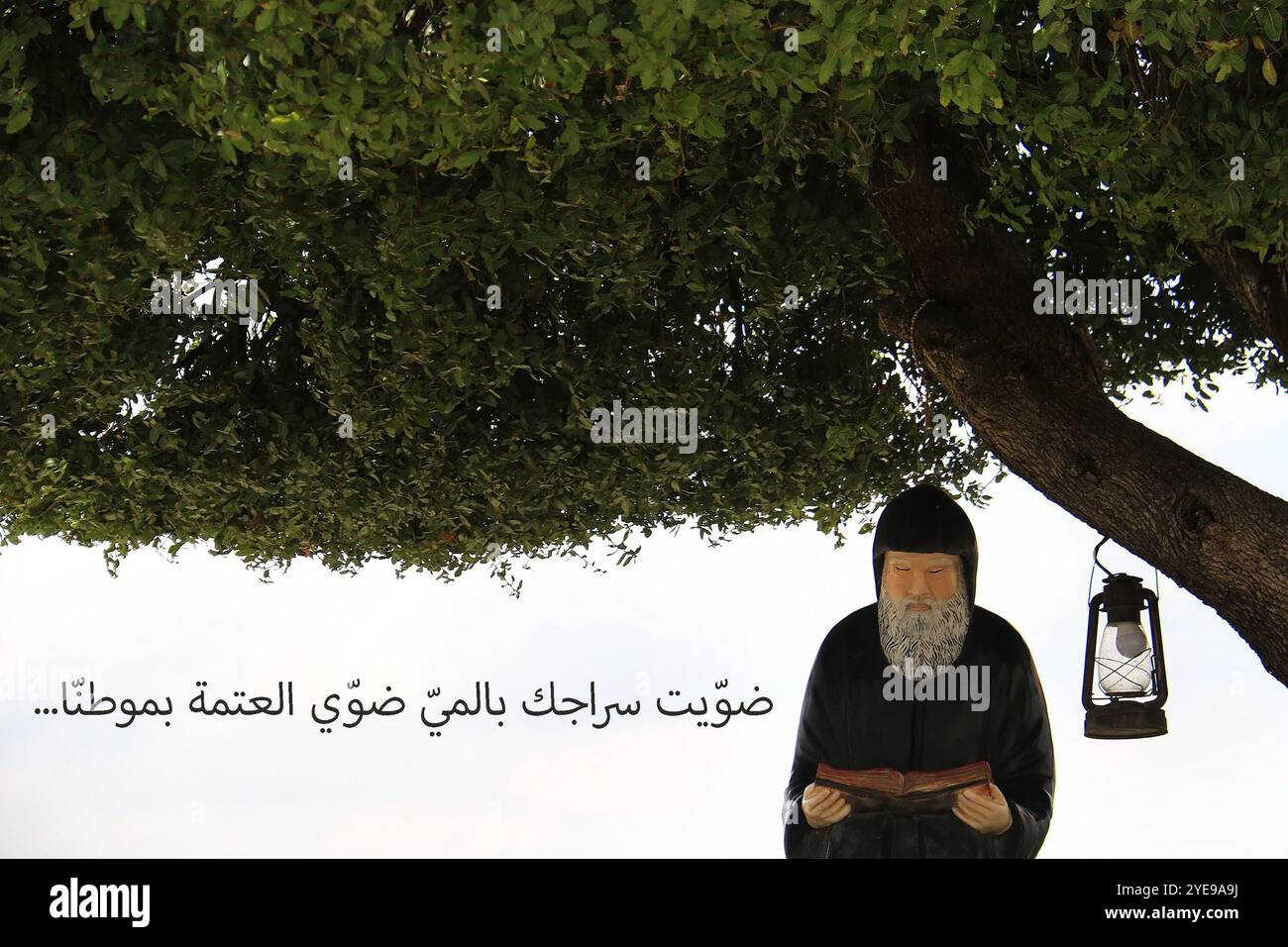 Une statue du Saint libanais Mar Charbel lisant la Bible, traduction du texte arabe : vous qui avez allumé votre lampe avec de l'eau, éclairez l'obscurité dans notre Banque D'Images