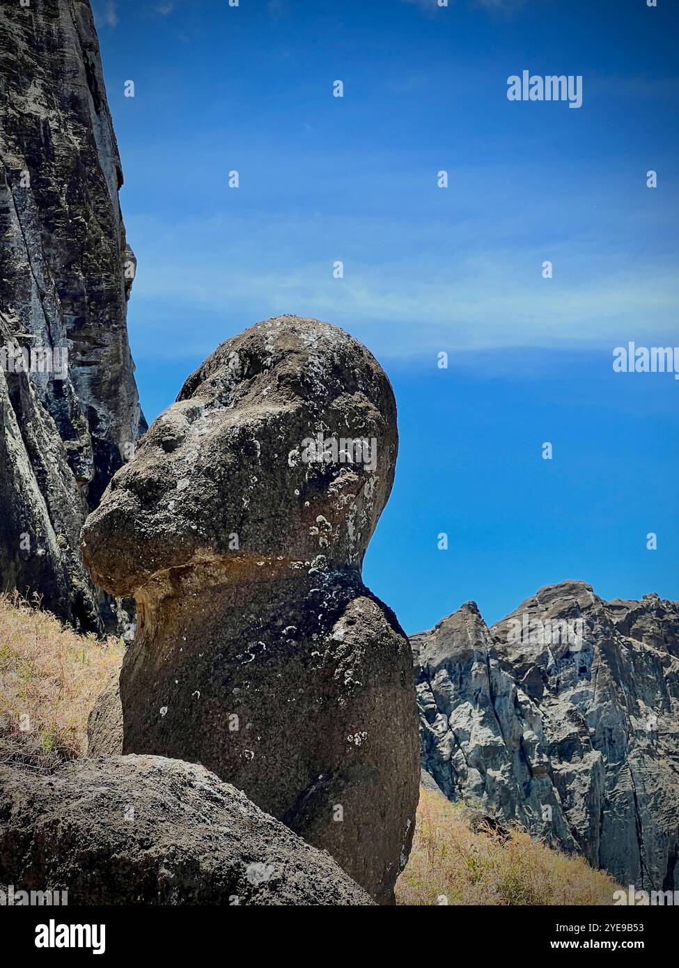 Une statue de moai solitaire sur l'île de Pâques, au Chili, posée contre des falaises accidentées et un ciel bleu vif. Ce site classé au patrimoine mondial de l’UNESCO reflète celui de Rapa Nui - Image de stock capturée avec un smartphone