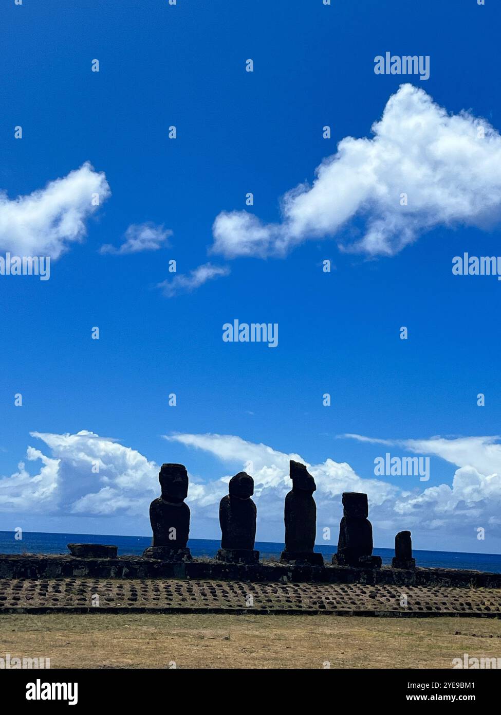 Silhouette de statues Moai emblématiques sur l'île de Pâques (Rapa Nui), au Chili, sur un ciel bleu vif et un horizon océanique, symbolisant l'ancienne Polynésie Banque D'Images