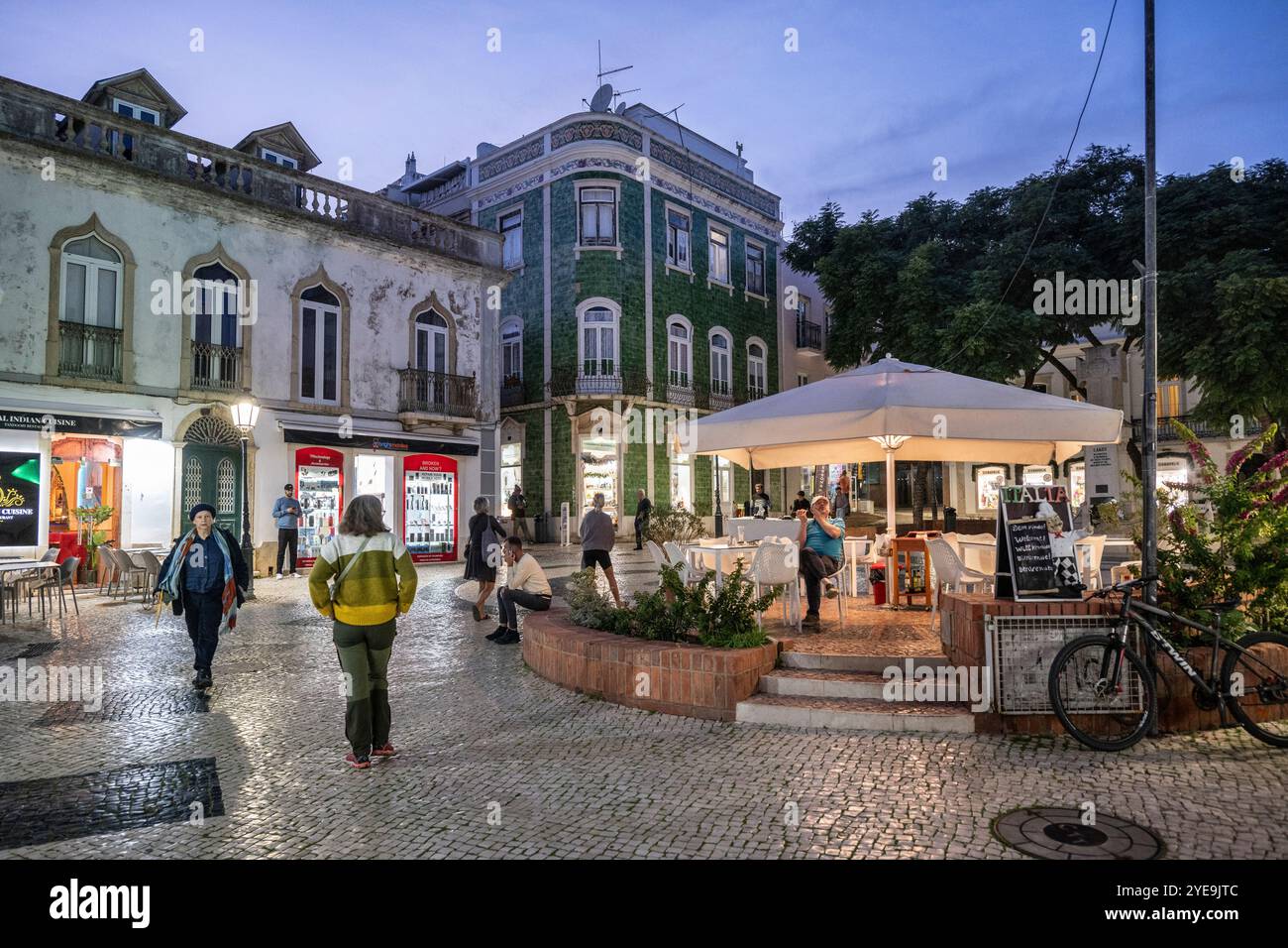 Les gens apprécient une place de la ville au crépuscule dans la ville côtière de Lagos. Lagos est une ville de la région de l'Algarve au sud du Portugal. Il est connu pour son mur... Banque D'Images