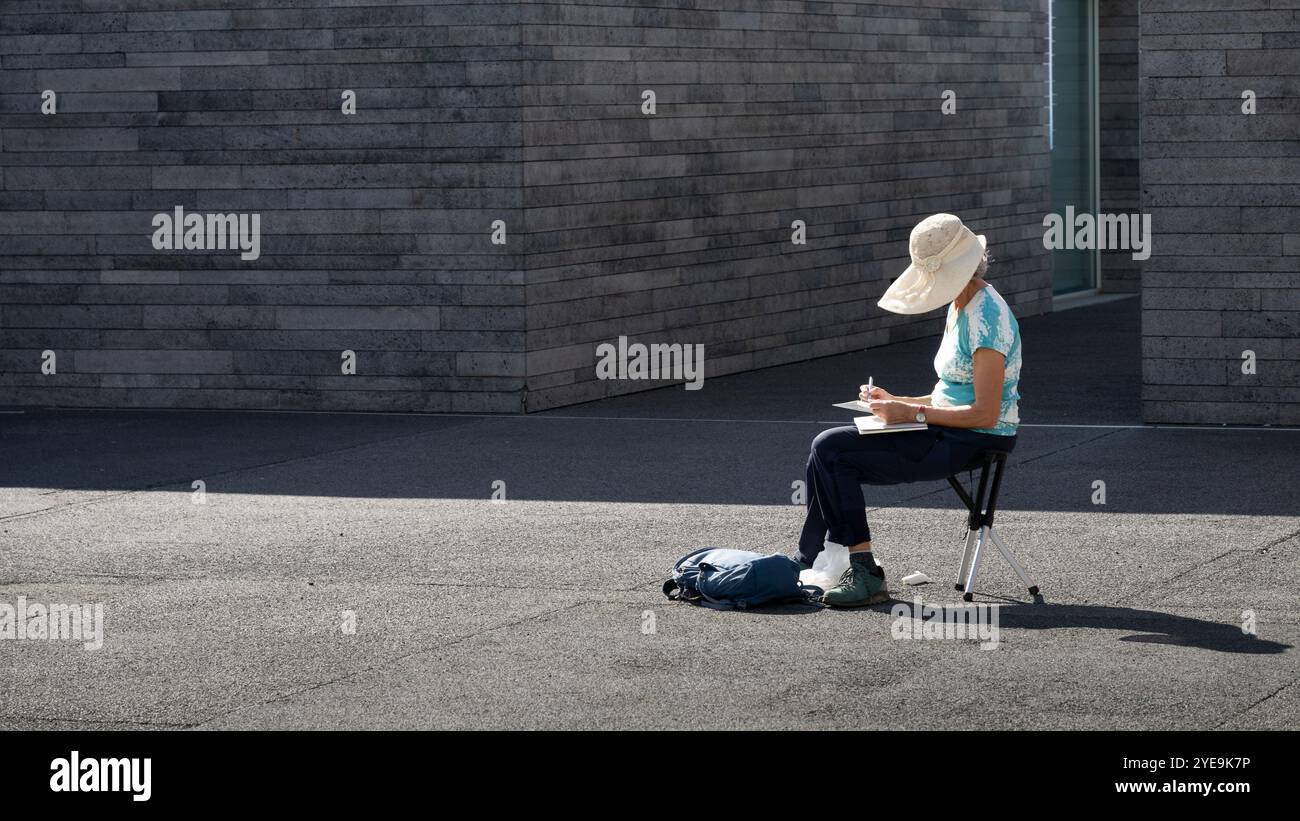 Femme assise sur un tabouret dessinant des œuvres d'art à la lumière du soleil avec un grand chapeau à bord sur l'île de Madère, Portugal ; Calheta, Madère, Portugal Banque D'Images