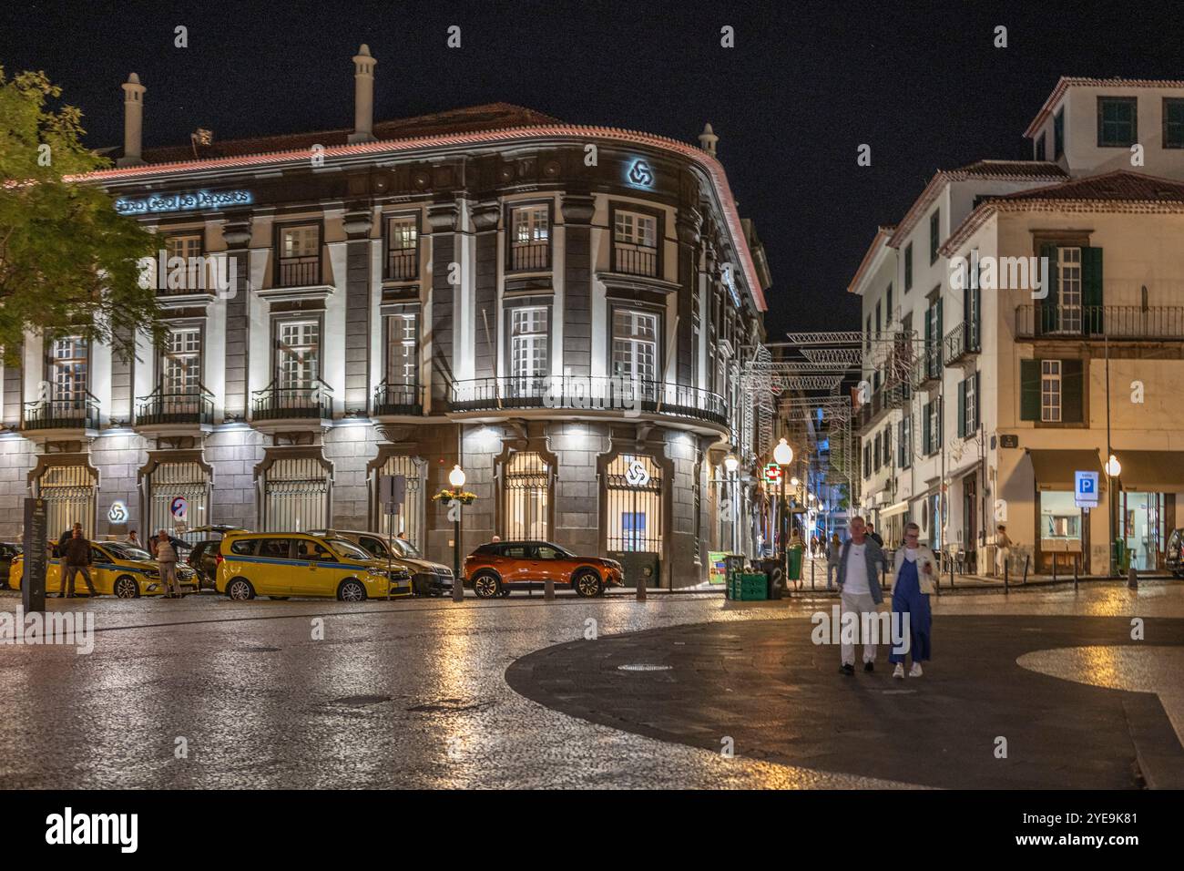Les piétons traversent une place de la ville avec des bâtiments illuminés la nuit à Funchal sur l'île de Madère, Portugal ; Funchal, Madère, Portugal Banque D'Images