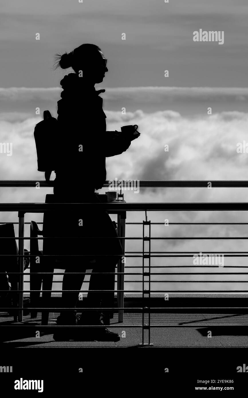 Image en noir et blanc d'une femme silhouette portant une tasse de café le long de la passerelle au-dessus des nuages à la randonnée Pico do Arieiro, São Roque do Faial Banque D'Images