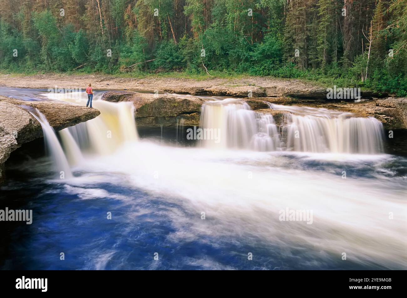 Femme se tient debout sur un rebord rocheux surplombant Coral Falls dans le parc territorial de Sambaa Deh Falls dans les Territoires du Nord-Ouest du Canada Banque D'Images