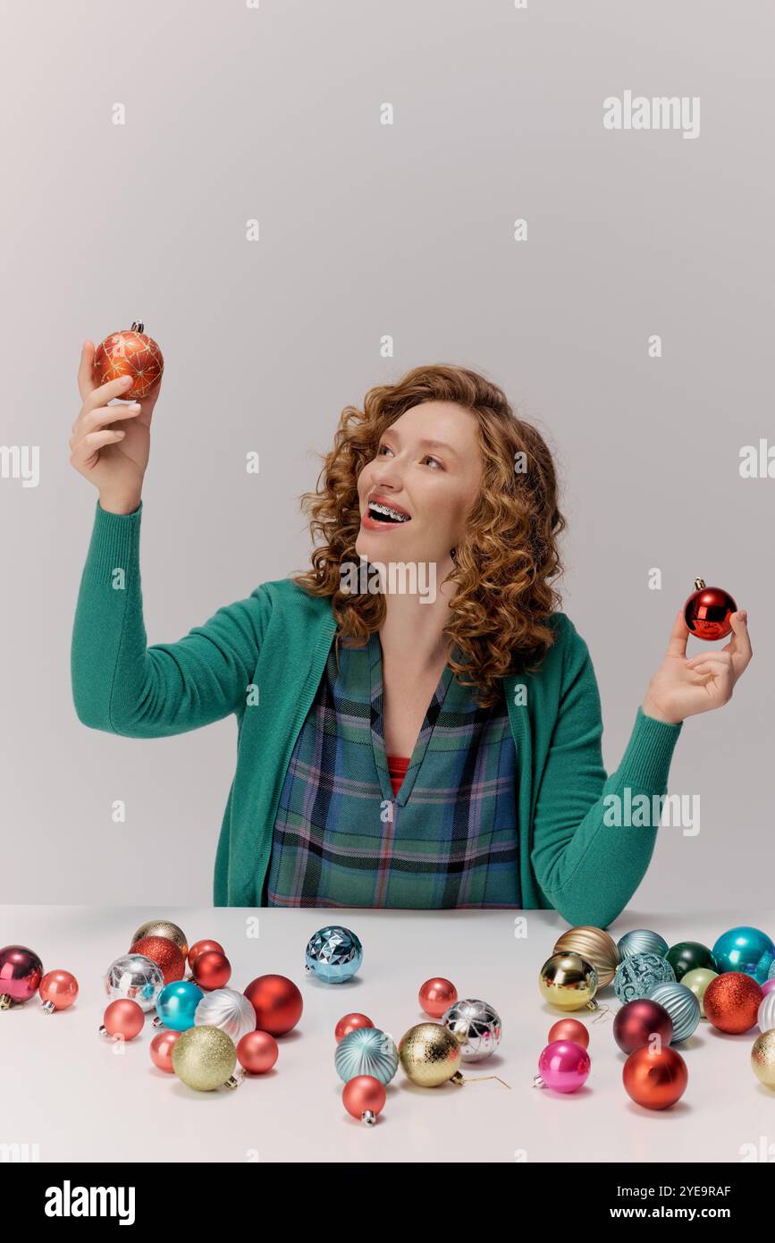 Une jeune femme joyeuse choisit joyeusement des ornements festifs parmi les décorations colorées de vacances. Banque D'Images