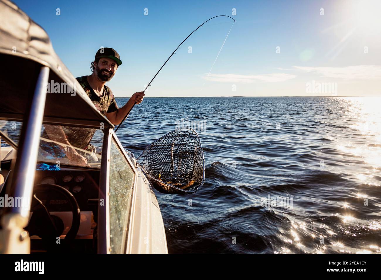 L'homme attrape un poisson d'un bateau pendant le temps sur un lac ; Alberta Beach, Alberta, Canada Banque D'Images