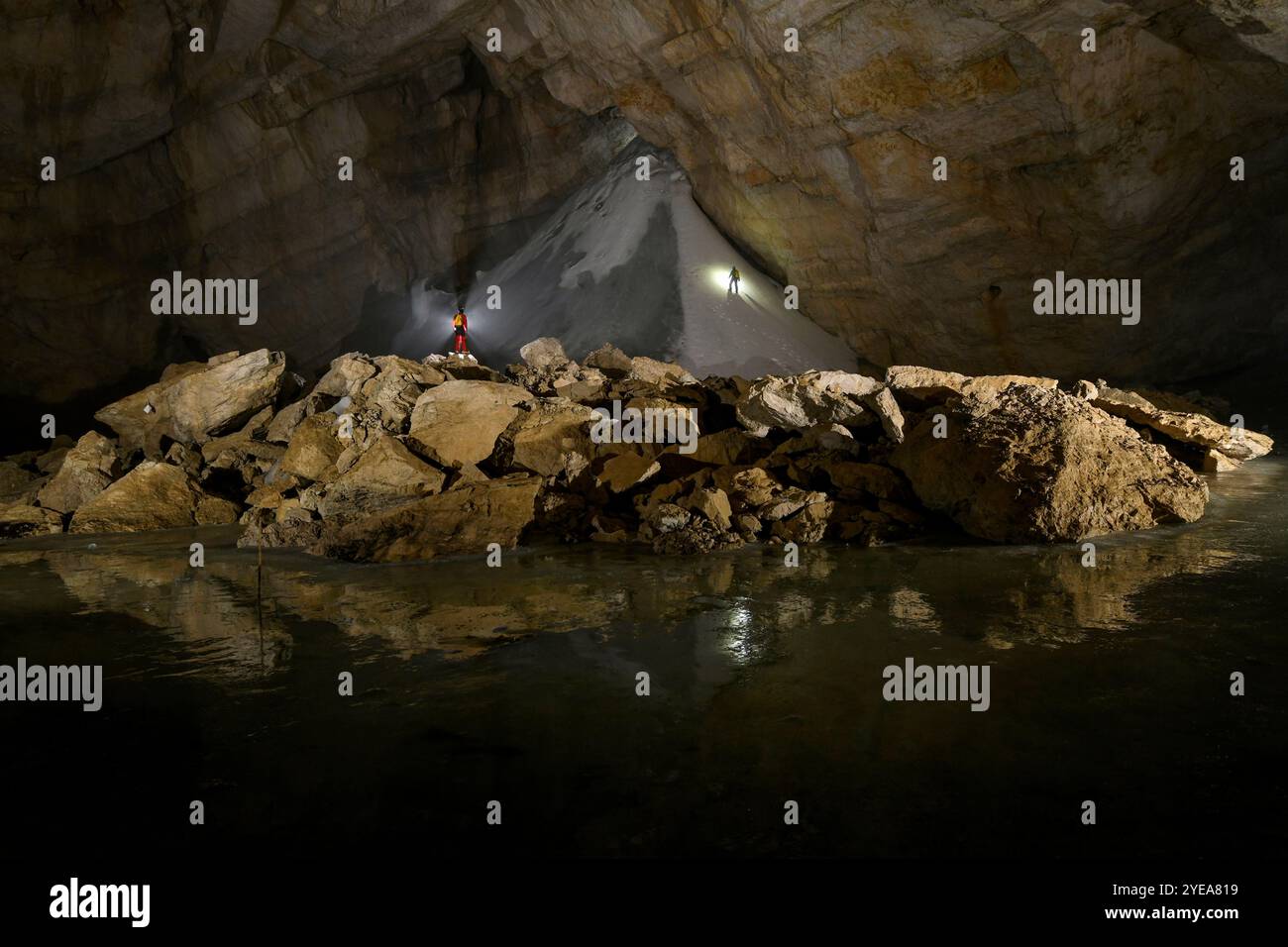 Des cavaliers en rappel explorant les formations de glace dans les grottes des Alpes européennes, menacées par le réchauffement climatique. Un lac d'eau de fonte est dans le for... Banque D'Images