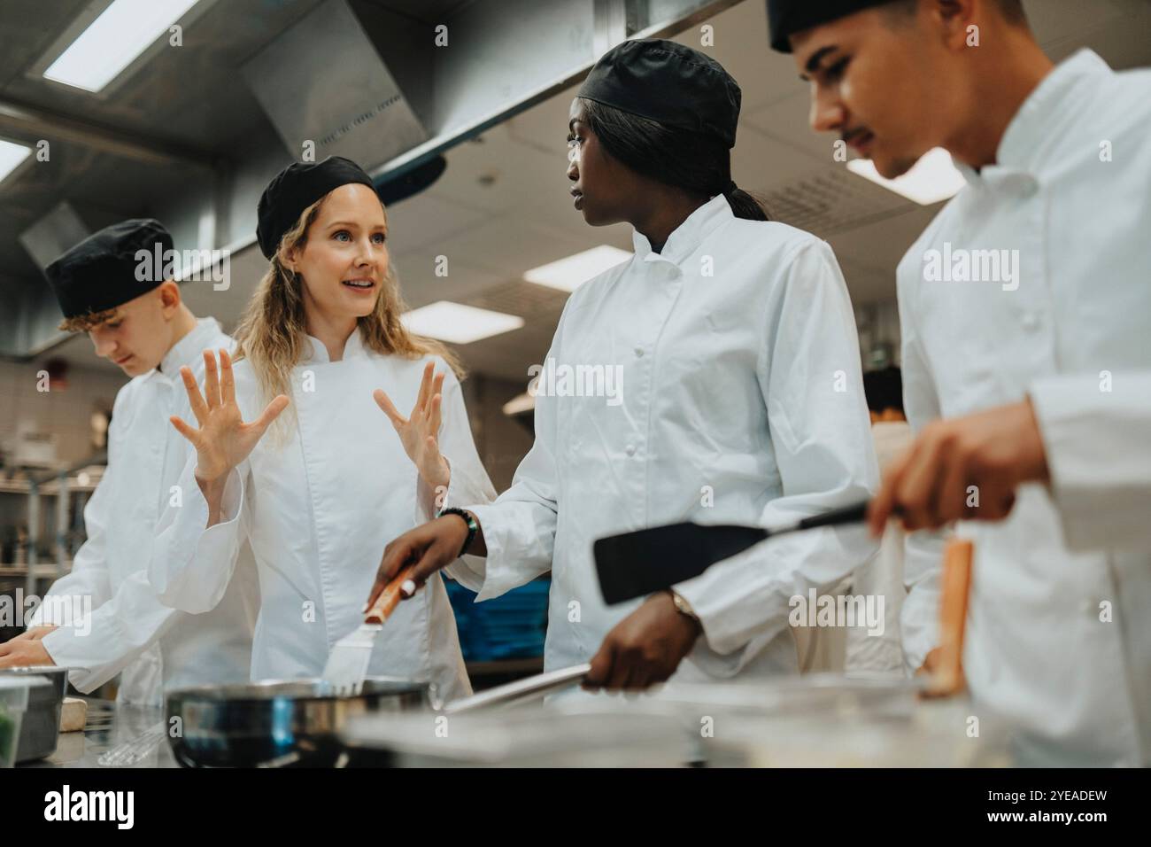 Enseignant faisant des gestes tout en guidant les stagiaires masculins et féminins à l'école culinaire Banque D'Images