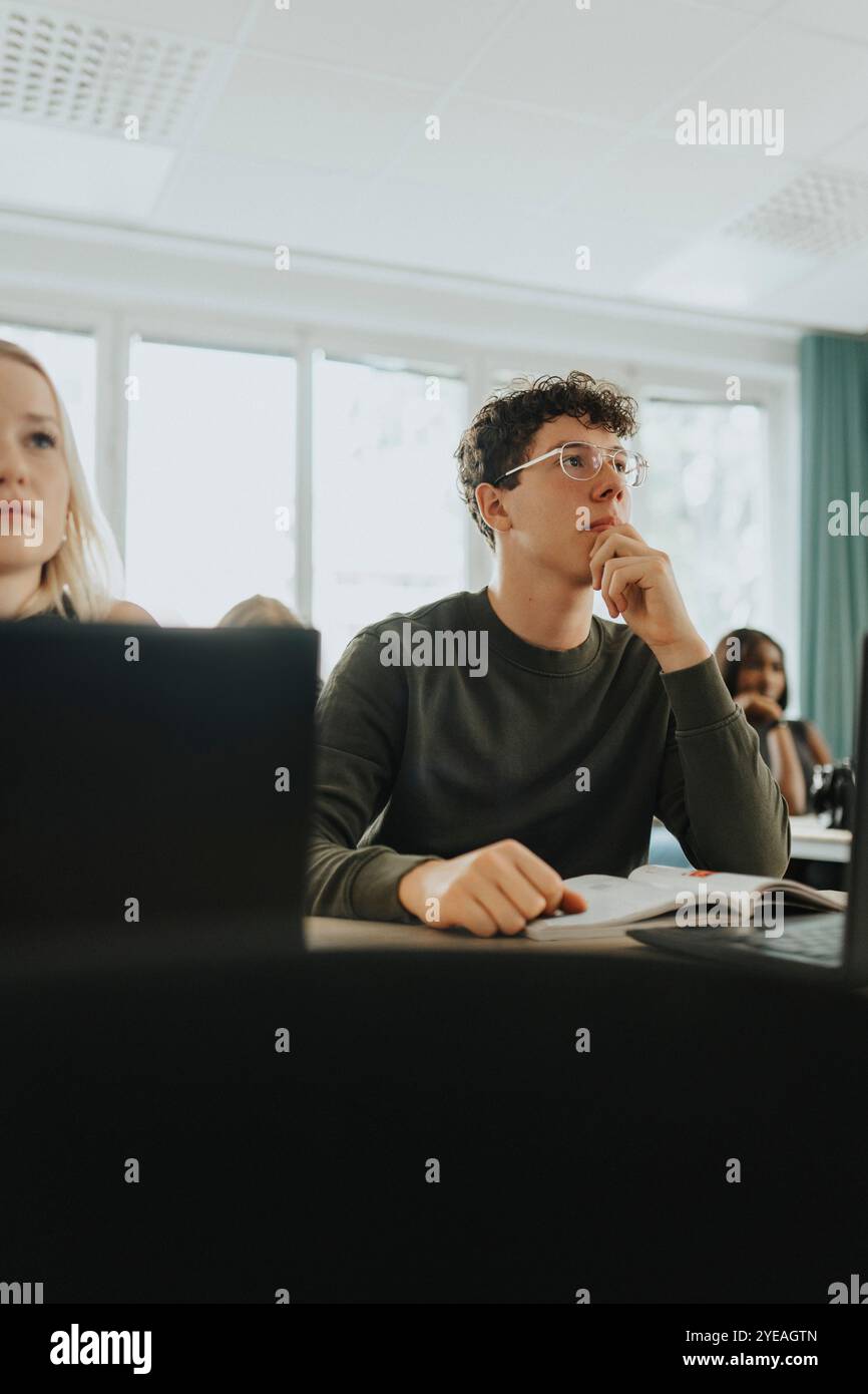 Adolescent assis avec la main sur le menton par une amie femelle en classe Banque D'Images