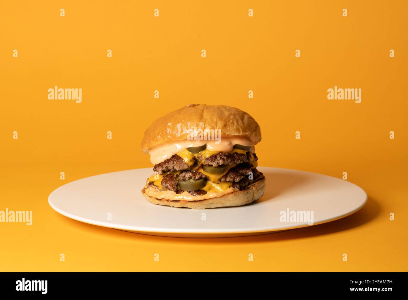 Délicieux cheeseburger, double cheeseburger avec sauce maison et jalapeno sur plaque blanche sur fond jaune Banque D'Images Délicieux cheeseburger, double cheeseburger avec sauce maison et jalapeno sur plaque blanche sur fond jaune Banque D'Images