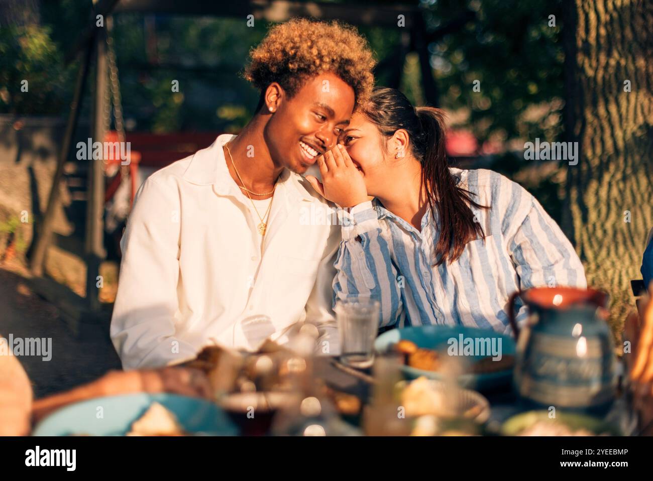 Femme chuchotant dans l'oreille d'un ami masculin assis à la table à manger pendant le dîner Banque D'Images