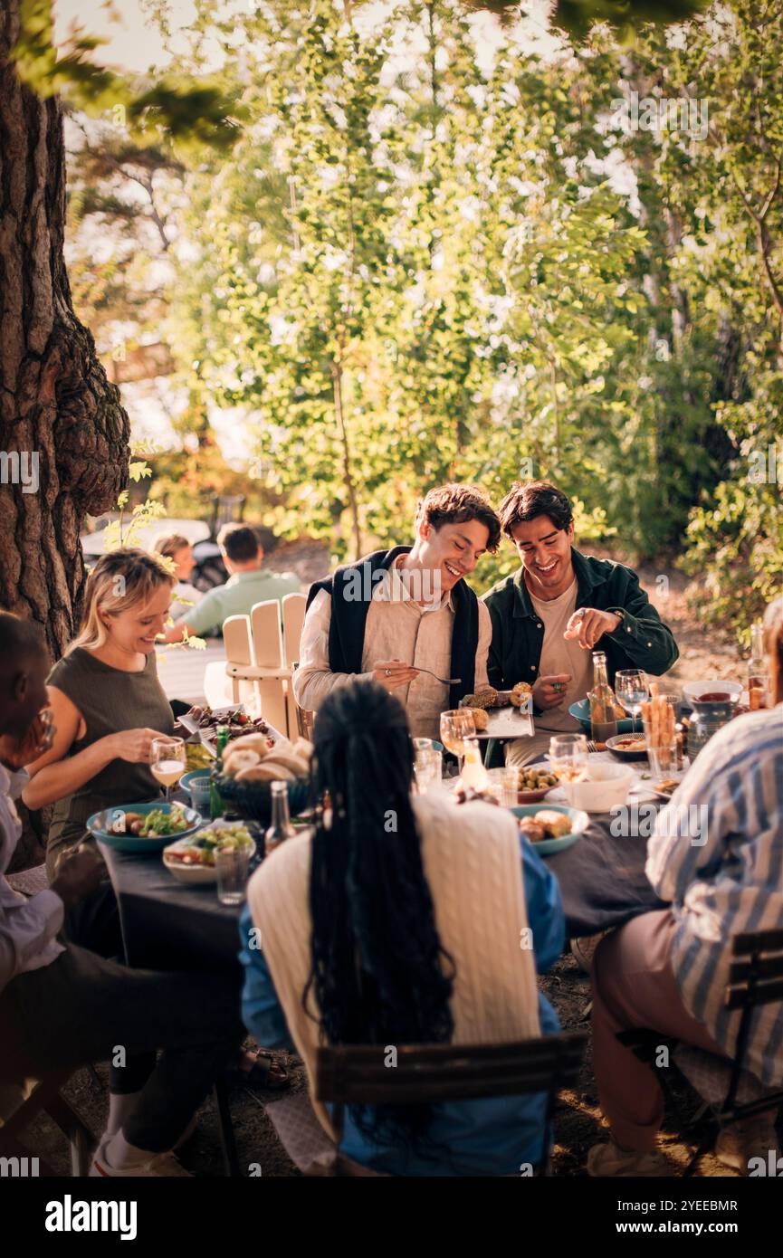 Heureux groupe d'amis masculins et féminins ayant de la nourriture assis à la table à manger pendant le dîner Banque D'Images