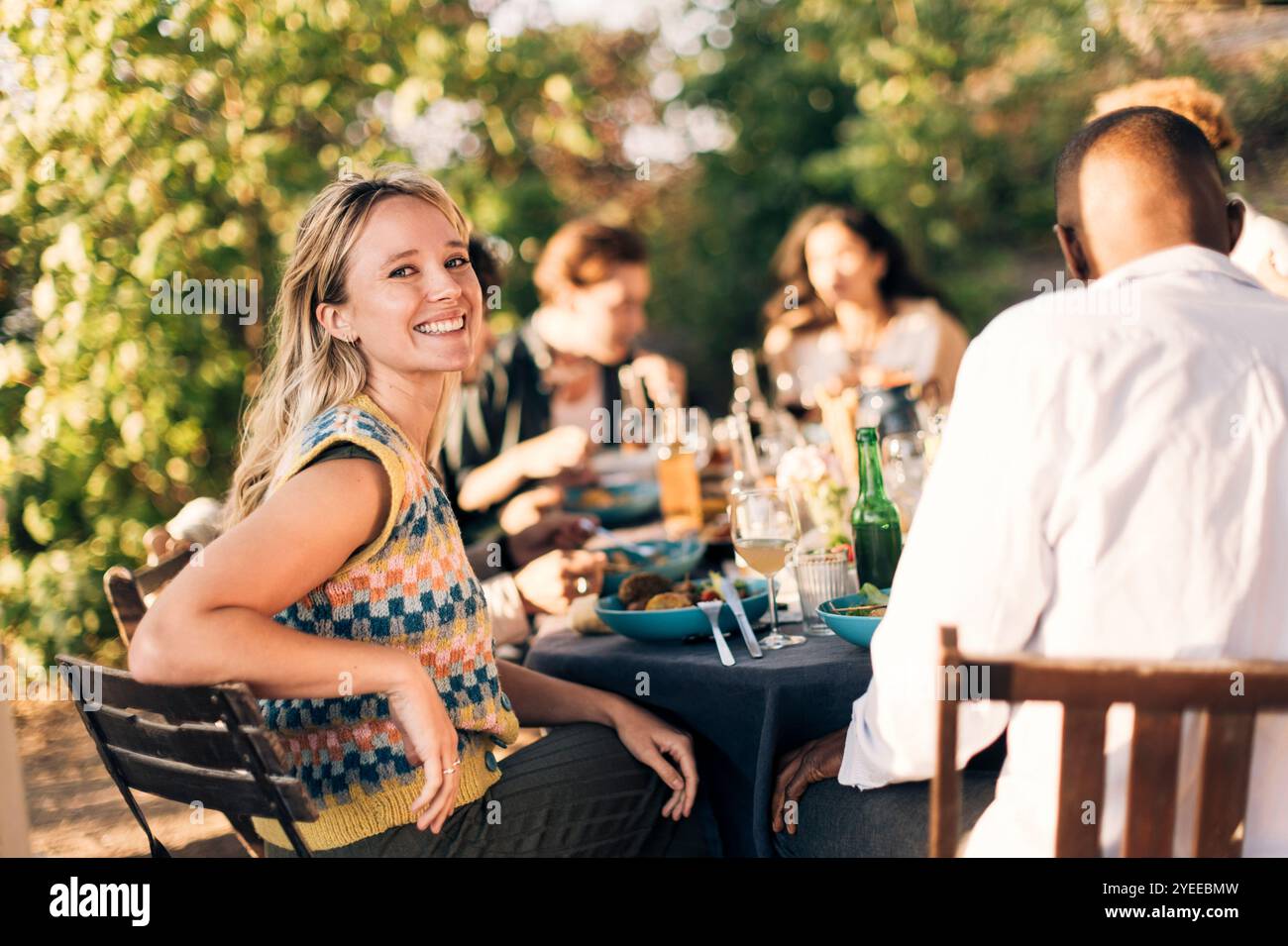 Portrait de vue de côté d'une femme souriante assise sur une chaise avec des amis pendant le dîner Banque D'Images