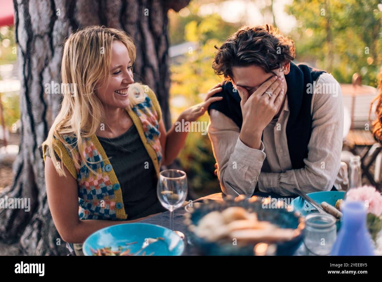 Femme souriante assise avec un ami masculin riant à la table à manger pendant le dîner Banque D'Images