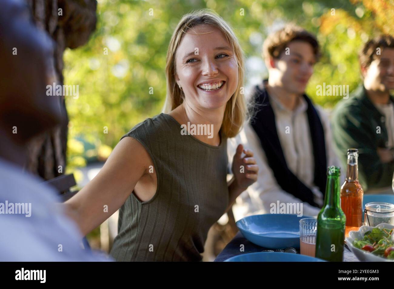 Femme heureuse appréciant avec des amis tout en étant assis à la table à manger pendant le dîner dans la cour arrière Banque D'Images