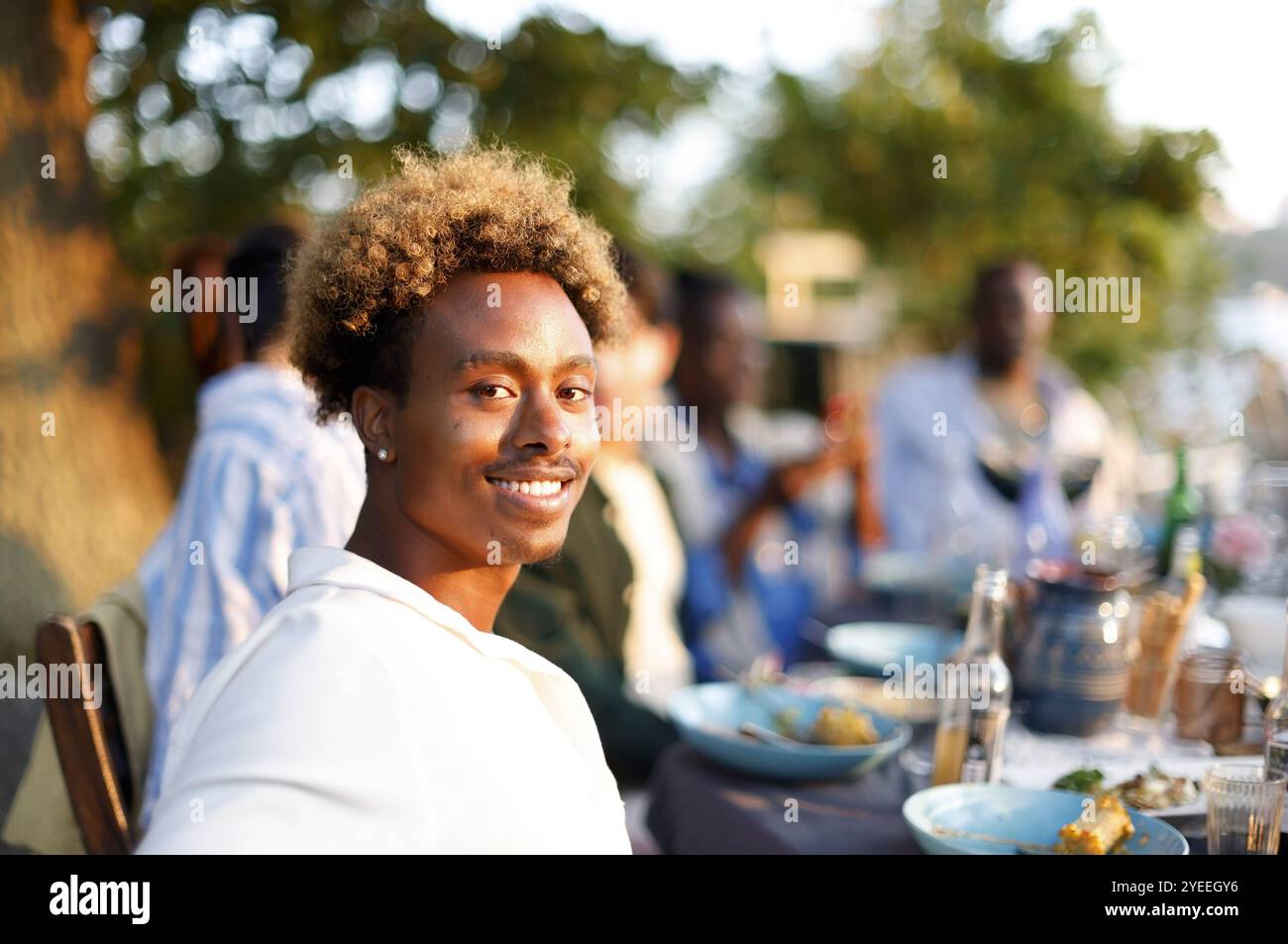 Portrait vue de côté d'un homme souriant avec des cheveux bouclés assis à la table à manger pendant le dîner Banque D'Images