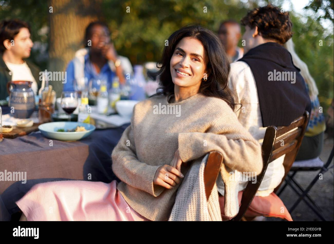 Portrait d'une femme souriante assise sur une chaise avec des amis appréciant pendant le dîner dans la cour arrière Banque D'Images