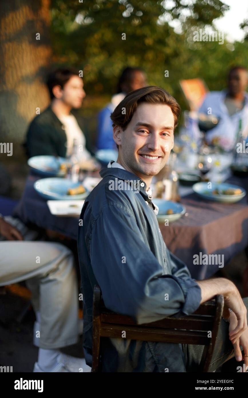 Portrait de jeune homme souriant avec des amis célébrant pendant le dîner dans la cour arrière Banque D'Images