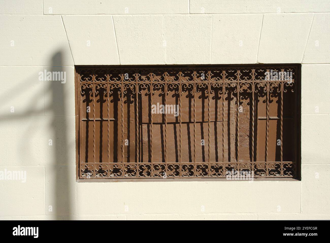 Vieux fer forgé isolé rouillé brun près du côté d'un mur de bloc ensoleillé clair. Ombre du poteau téléphonique et des fils à gauche. Vue large n° p Banque D'Images